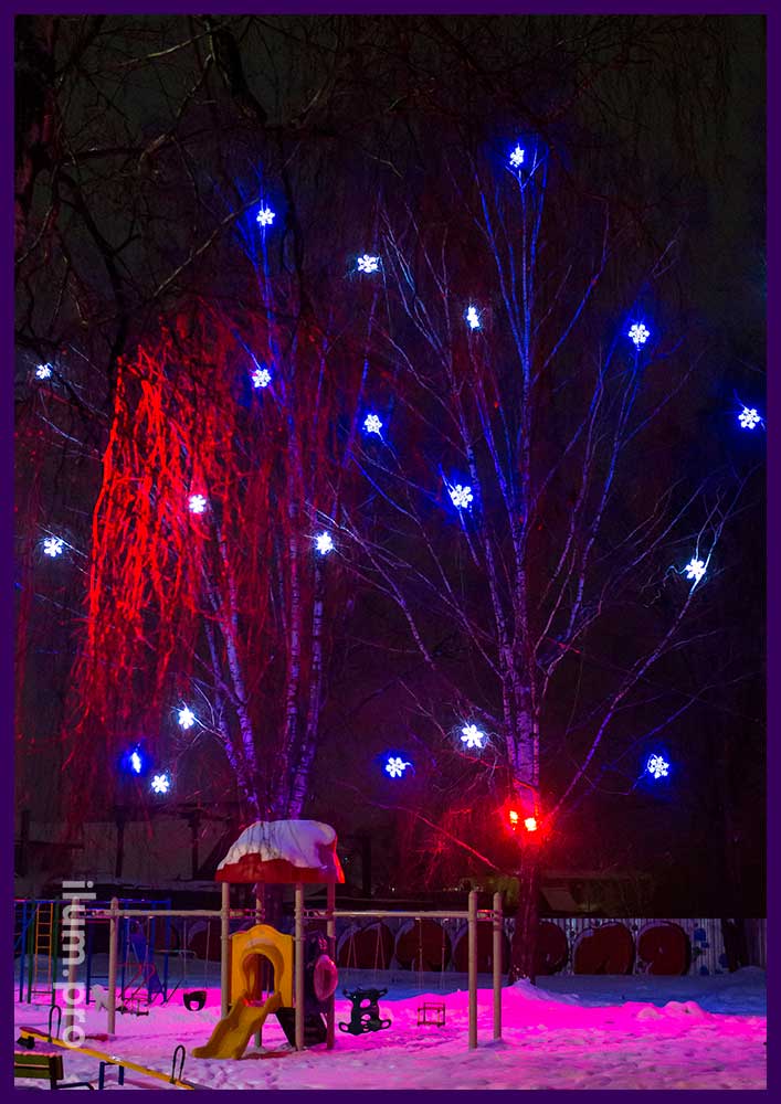 Новогодняя подсветка деревьев снежинками белого и синего цвета и разноцветными светильниками