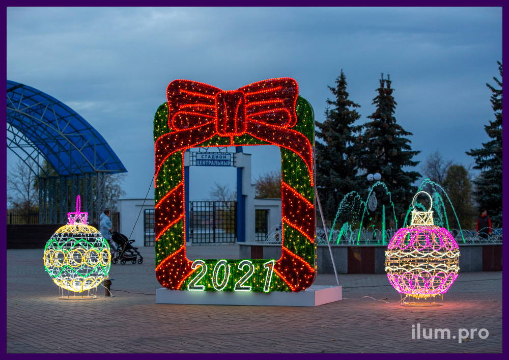 Уличная фотозона в форме рамки с бантом из мишуры и гирляндами на Новый год