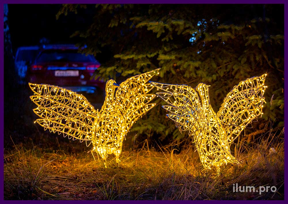 Два светодиодных гуся из металла с гирляндами рядом с ёлками в парке на Новый год