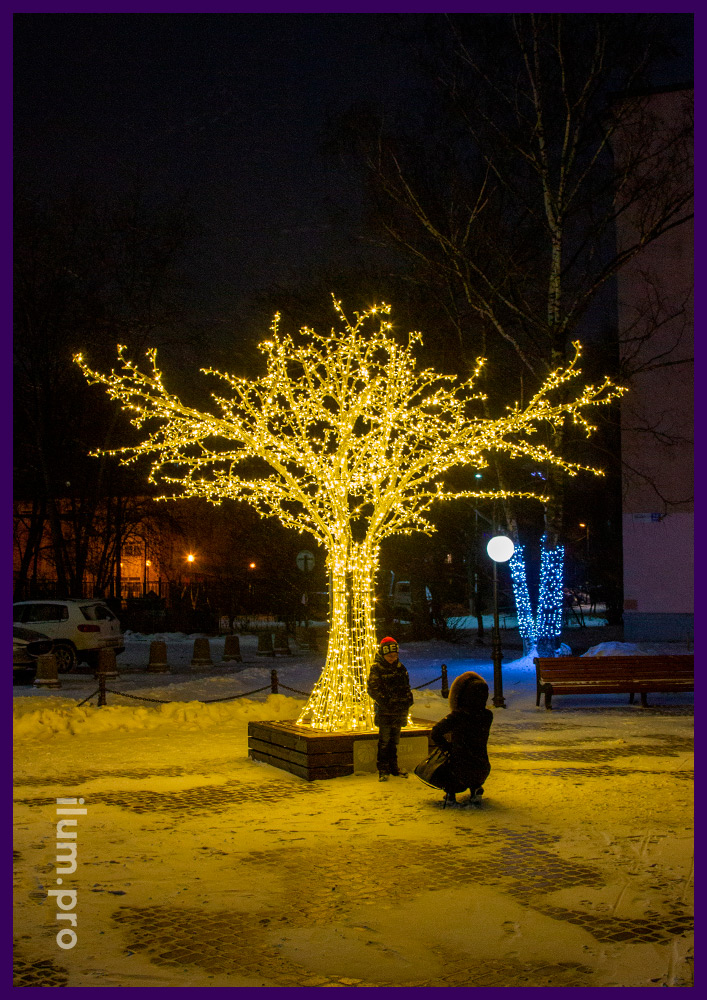 Тёпло-белое дерево с подсветкой гирляндами и лавочкой в основании на площади Владимира