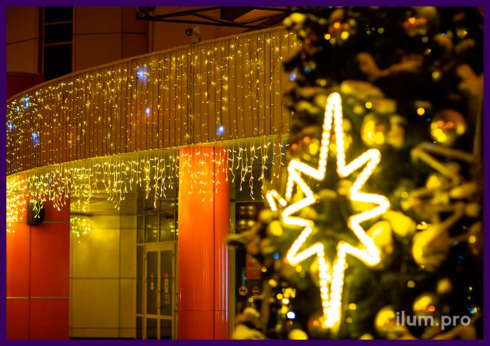 Новогоднее украшение уличной ёлки перед торговым центром золотыми шарами и светящимися звёздами
