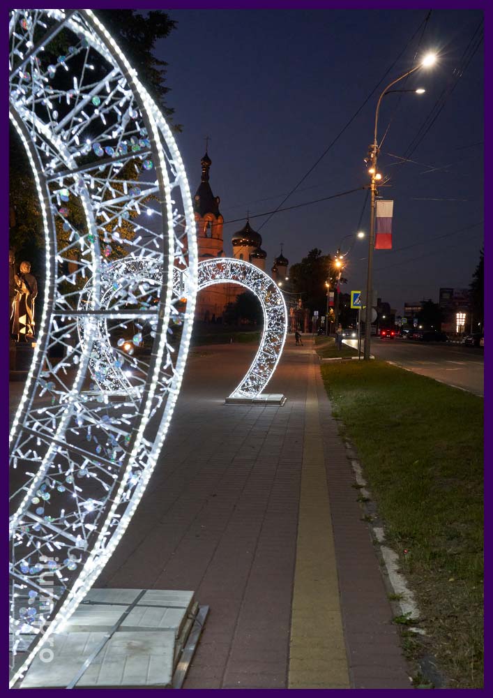 Пара арок белого цвета с подсветкой уличными гирляндами на тротуаре в Раменском