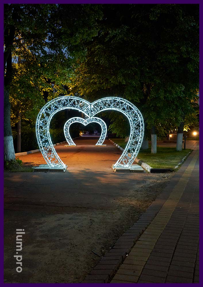 Пара декоративных арок в форме светящихся сердец с белыми гирляндами и серебристыми блёстками