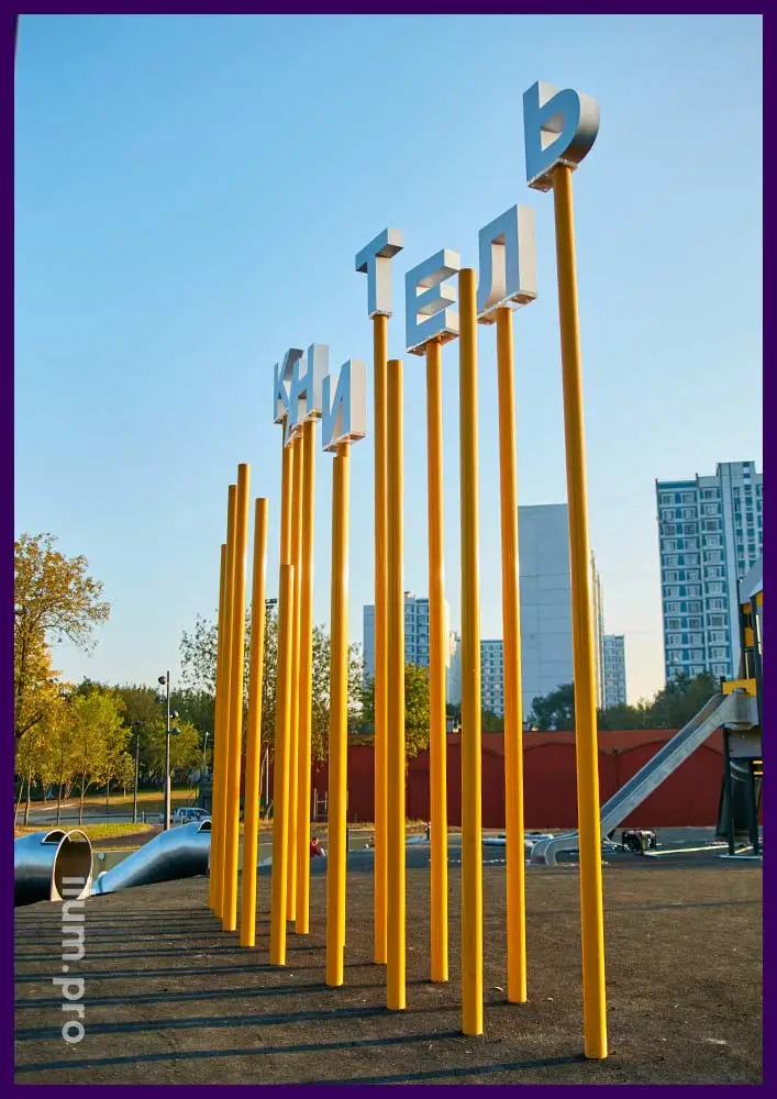 Канитель - надпись из акриловых букв и жёлтых, металлических столбов на детской площадке